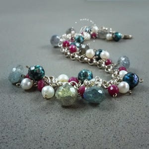 May include: A handmade bracelet with a silver chain and a variety of gemstone beads. The beads include pearls, ruby, and iridescent blue, green, and grey stones. The bracelet is labelled "Marie Wu Designs".