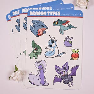 May include: A set of eight stickers featuring different dragon-type Pokemon. The stickers are printed on white paper with a blue border and the text "Dragon Types" at the top. The stickers feature a variety of Pokemon, including a blue dragon, a green dragon, a purple dragon, a pink dragon, a blue snake, a green snake, a purple bat, and a red apple.