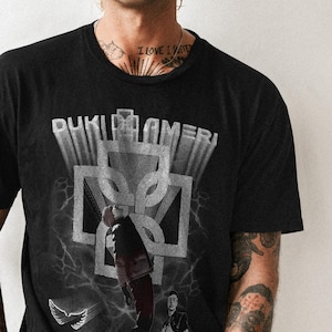 May include: Black t-shirt with a white graphic print of a person in a black outfit with the text "DUKI" and "DUKI LAMERI" on the front.
