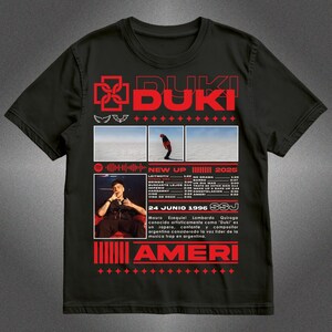 May include: Black t-shirt with a red graphic of the word "DUKI" and a red cross symbol. The graphic also includes a photo of a person, a list of song titles, and the text "NEW UP 2025". The text "24 JUNIO 1996 SSJ" is also included in the graphic.