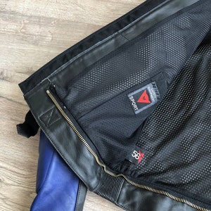 K&ouml;nnte beinhalten: Schwarze Leder-Motorradjacke mit blauem Futter und einem Dainese Sport-Label. Die Jacke hat einen Rei&szlig;verschluss und ein Mesh-Futter.