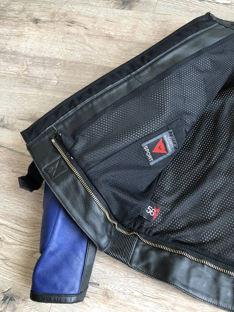 K&ouml;nnte beinhalten: Schwarze Leder-Motorradjacke mit blauem Futter und einem Dainese Sport-Label. Die Jacke hat einen Rei&szlig;verschluss und ein Mesh-Futter.