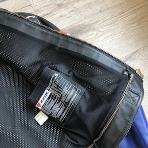 K&ouml;nnte beinhalten: Schwarze Leder-Motorradjacke mit einem blau-orangen Farbblock-Design. Die Jacke hat einen Rei&szlig;verschluss und ein Mesh-Futter. Das Etikett im Inneren der Jacke lautet "Dainese".