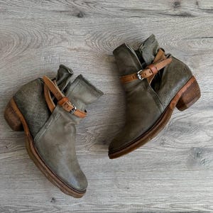 May include: A pair of gray leather ankle boots with brown leather straps and buckles. The boots have a slightly distressed look and a chunky heel.