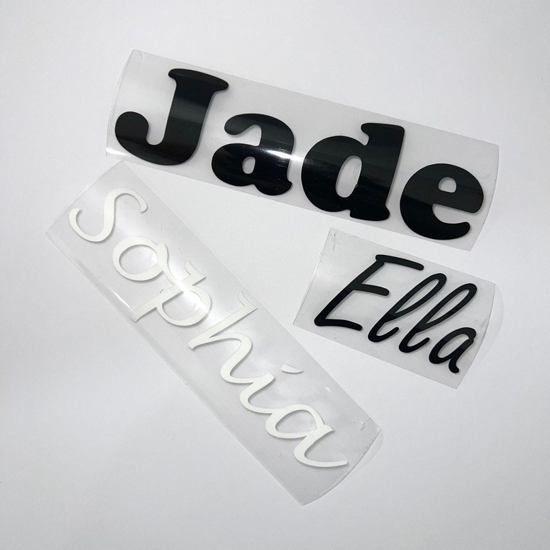 May include: Three name decals: "Jade" in black, "Sophia" in white, and "Ella" in black. The names are in a cursive font, each on a clear backing. Ideal for personalizing items.