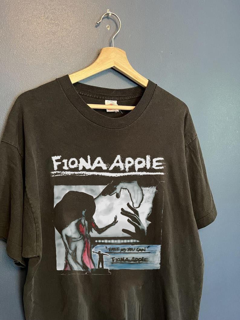 Może przedstawiać: Czarny T-shirt z białym nadrukiem okładki albumu Fiony Apple "Fast as You Can". Okładka albumu przedstawia czarno-białą ilustrację kobiety w czerwonej sukience.