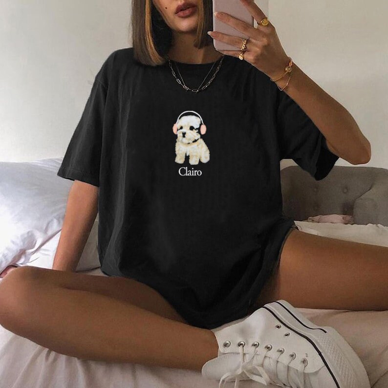 May include: Black oversized t-shirt featuring a graphic of a white dog wearing headphones with the word "Clairo" printed beneath.