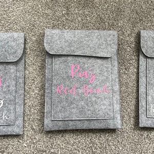 以下が含まれることがあります： フラップクロージャー付きの3つの灰色のフェルトブックカバー。各カバーには、異なる刺繍の虹のデザインとテキストがあります。最初のカバーには「Brooke's Red Book」、2番目には「Pia's Red Book」、3番目には「Rory's Red Book」と書かれています。