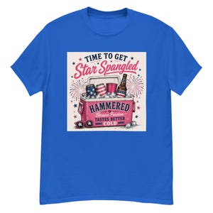Peut inclure: T-shirt bleu royal avec un motif d'une glacière rose contenant des canettes, des gobelets et une bouteille, avec le texte "TIME TO GET Star Spangled." La glacière porte le mot "HAMMERED" et la phrase "Because Freedom Tastes Better COLD."