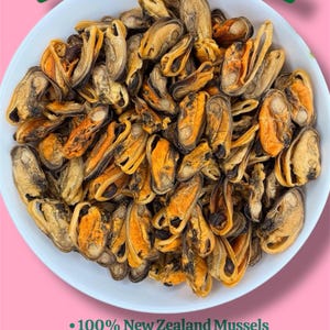 Op de afbeelding: Een witte kom gevuld met gedehydrateerde groenlipmosselen. De mosselen hebben een mix van bruine en oranje tinten. De tekst bovenaan luidt "Gedehydrateerde Groenlipmosselen". Hieronder staat "100% Nieuw-Zeelandse Mosselen", "Slechts één ingrediënt" en "Gewrichtsondersteuning Treat + Voor Actieve Honden."