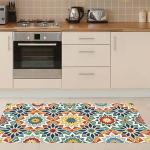 May include: A colorful geometric patterned rug with a starburst design in a kitchen setting. The rug features a repeating pattern of blue, orange, yellow, and green shapes. The kitchen has white cabinets, a stainless steel oven, and a microwave.