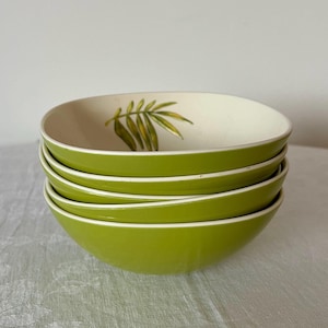 Op de afbeelding: Een stapel van vier groene keramische kommen. Elke kom heeft een witte binnenkant met een groen en geel bladerontwerp. De kommen hebben een gladde, glanzende afwerking en een witte rand.