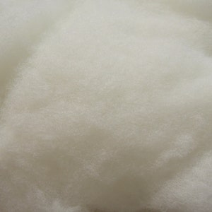 May include: Close-up of a pile of fluffy, off-white material. The texture appears soft and cloud-like, with a dense, interwoven structure. The material is evenly colored, suggesting a consistent composition. The image highlights the tactile quality of the material.