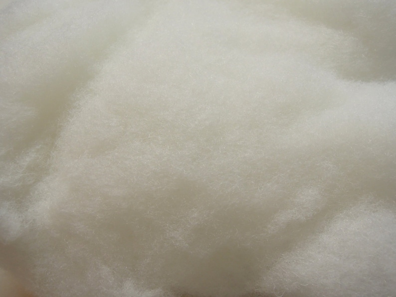 May include: Close-up of a pile of fluffy, off-white material. The texture appears soft and cloud-like, with a dense, interwoven structure. The material is evenly colored, suggesting a consistent composition. The image highlights the tactile quality of the material.