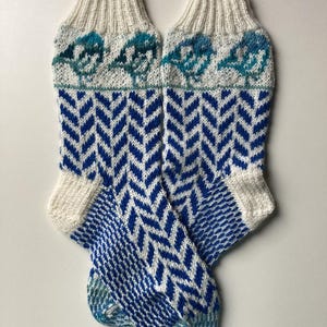 Op de afbeelding: Een paar witte en blauwe gebreide sokken met een chevron-patroon en een vogelontwerp aan de bovenkant.