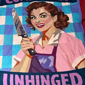 Peut inclure: Une couverture avec une illustration rétro d'une femme tenant un couteau, avec les mots "COMPLETELY UNHINGED" en texte violet. Le fond présente un motif à carreaux bleu et blanc. La femme porte une robe rose et un tablier violet.