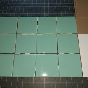 May include: A grid of twelve square, glossy, light mint green ceramic tiles arranged in three rows of four. Each tile features a smooth, reflective surface with straight edges, presented in a uniform layout to showcase the consistent color.