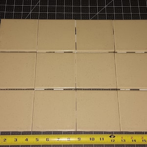May include: Twelve beige square tiles arranged in a grid, with a measuring tape along the bottom. Each tile is approximately 4 inches square. The tiles have a speckled surface and are suitable for home improvement projects.