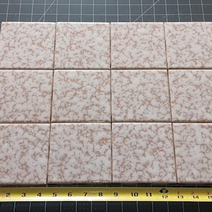 May include: Twelve beige and brown speckled tiles arranged in three rows of four. A yellow measuring tape shows the tiles are approximately 17 inches wide. The tiles have a glossy finish and are suitable for home improvement projects.