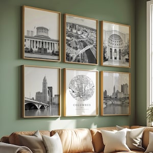 May include: Six framed black and white prints of Columbus, Ohio, hang on a green wall. The prints include architectural and city views, and a map of the city. A brown leather sectional sofa with pillows and a white coffee table are in the foreground.