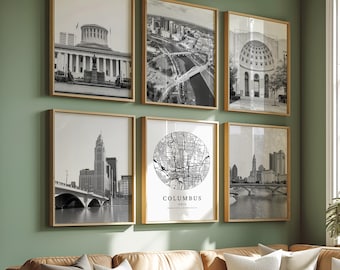 May include: Six framed black and white prints of Columbus, Ohio, hang on a green wall. The prints include architectural and city views, and a map of the city. A brown leather sectional sofa with pillows and a white coffee table are in the foreground.