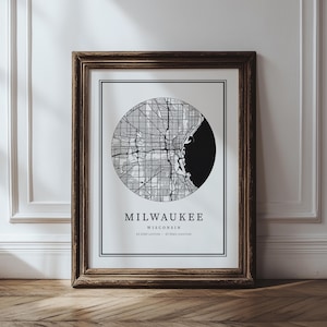 May include: Framed print featuring a black and white circular map of Milwaukee, Wisconsin. The city map is detailed with streets and a black silhouette of the shoreline. The print is in a dark brown wooden frame, with the city name and coordinates displayed below the map.