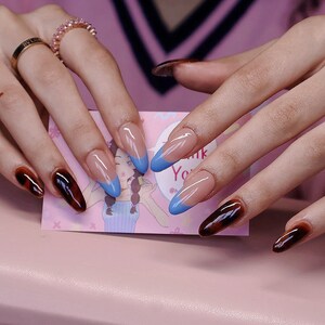 May include: Close-up of long, almond-shaped nails with a brown tortoiseshell design and a blue tip accent. The nails are painted with a clear base and a brown tortoiseshell design. The tips of the nails are painted with a bright blue colour.