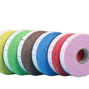 May include: A row of colorful rolls of double-sided adhesive tape. The rolls are in shades of yellow, green, brown, blue, red, and pink. Each roll has a white backing with small square adhesive sections.