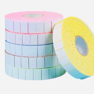May include: A stack of colorful label rolls. The rolls are pink, blue, and green, with white labels and colored borders. A yellow roll with white labels and blue borders is leaning against the stack.