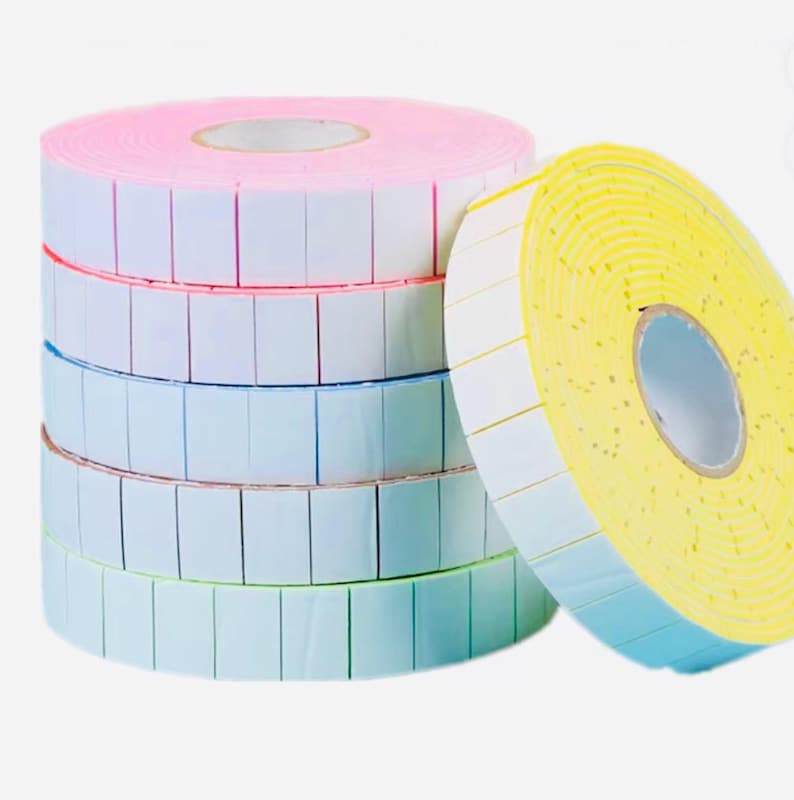 May include: A stack of colorful label rolls. The rolls are pink, blue, and green, with white labels and colored borders. A yellow roll with white labels and blue borders is leaning against the stack.