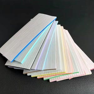 May include: A fan of colorful, textured, rectangular strips with various colored edges. The strips are arranged in a fanned-out pattern, showcasing a range of pastel and bright colors, including blue, green, pink, and yellow.