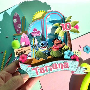 Puede incluir: Adorno de pastel de cumplea&ntilde;os colorido y en capas con los personajes Stitch y Lilo de la pel&iacute;cula Lilo & Stitch. El adorno incluye una pancarta con el nombre "Tatiana", una palmera con el n&uacute;mero "10" y elementos tem&aacute;ticos de playa.
