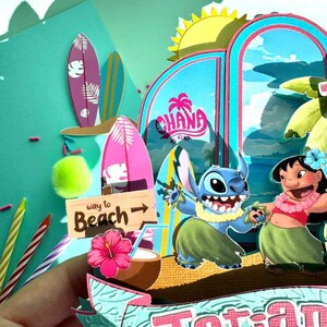 Puede incluir: Una colorida escena de manualidades de papel con los personajes Stitch y Lilo & Stitch. La escena incluye tablas de surf, un letrero que dice "Way to Beach" y la palabra "Ohana". El tema general es tropical y de playa.