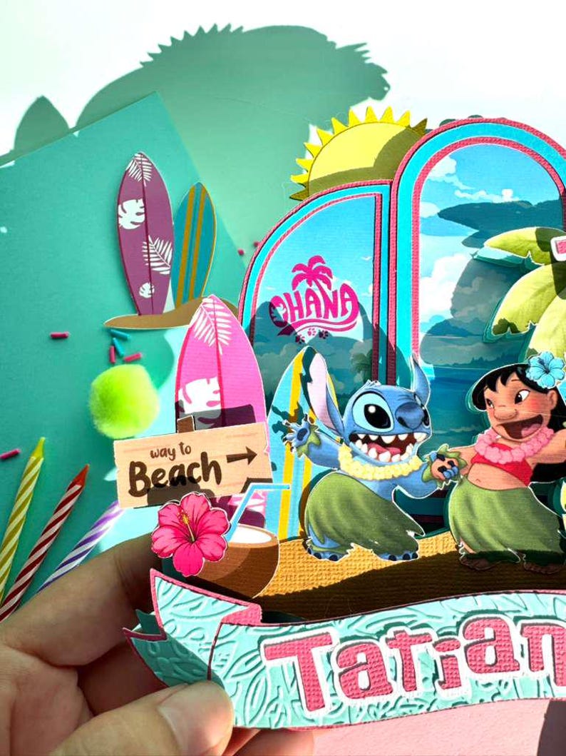 Puede incluir: Una colorida escena de manualidades de papel con los personajes Stitch y Lilo & Stitch. La escena incluye tablas de surf, un letrero que dice "Way to Beach" y la palabra "Ohana". El tema general es tropical y de playa.
