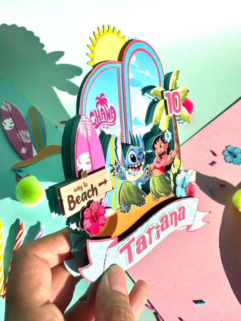 Puede incluir: Un adorno para tarta de cumplea&ntilde;os colorido y en capas con los personajes Stitch y Lilo de la pel&iacute;cula Lilo & Stitch. El dise&ntilde;o incluye una pancarta con el nombre "Tatiana", un letrero de "Way to Beach" y el n&uacute;mero "10".