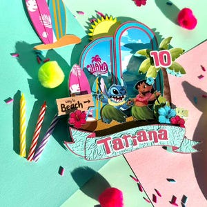 Puede incluir: Adorno de pastel de cumplea&ntilde;os colorido con tem&aacute;tica tropical con los personajes Stitch y Lilo. El dise&ntilde;o incluye tablas de surf, palmeras y el nombre "Tatiana" en una pancarta. Tambi&eacute;n se muestra el n&uacute;mero "10".