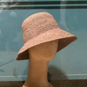 May include: A light brown sun hat with a wide brim, displayed on a mannequin head. The hat has a woven texture and a slightly rounded crown. The mannequin is a neutral tan colour.