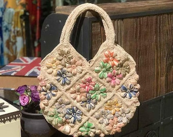 May include: A crocheted tote bag with a round shape and a floral design. The bag is made of natural fibers and features colorful flowers in shades of pink, blue, green, and yellow.
