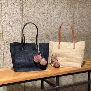 Pode incluir: Duas bolsas tote de palha com detalhes de pompons. A bolsa à esquerda é preta e tem alças pretas. A bolsa à direita é bege e tem alças marrons.