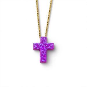 Puede incluir: Collar con cadena dorada y colgante de cruz morada. La cruz presenta un patrón moteado en tonos morados. La cadena es fina y brillante.