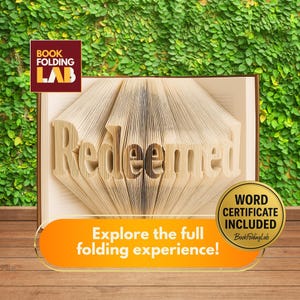 May include: A book with the word "Redeemed" folded into the pages. The book is open, revealing the sculpted word. The image includes the text "Explore the full folding experience!" and "WORD CERTIFICATE INCLUDED". The background features a green wall and a wooden surface.