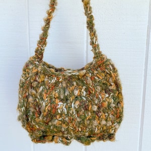 May include: A crocheted handbag with a green, brown, orange, and white color scheme. The bag has a single strap and a slouchy, casual shape.