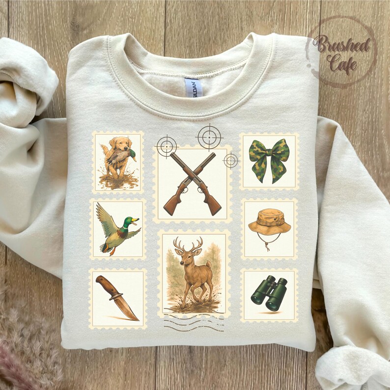 Peut inclure: Sweat-shirt cr&egrave;me avec un motif sur le th&egrave;me de la chasse. Le design comprend des illustrations d'un chien avec un canard, de fusils crois&eacute;s, d'un n&oelig;ud, d'un chapeau, d'un couteau, d'un cerf et de jumelles, le tout dans des cadres en forme de timbre-poste.