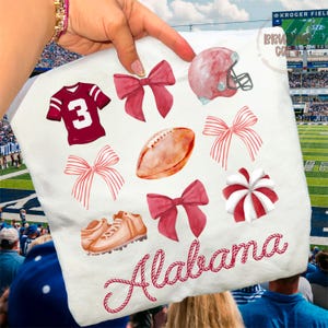 May include: White fabric featuring watercolor illustrations of a football jersey with the number 3, bows, a football, a helmet, cleats, and a peppermint wheel. The word "Alabama" is written in red script.