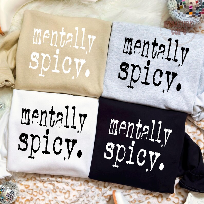 Puede incluir: Cuatro sudaderas en beige, gris, blanco y negro, cada una con la frase "mentally spicy" en una fuente blanca desgastada. Las sudaderas est&aacute;n dobladas y dispuestas juntas, mostrando el dise&ntilde;o.