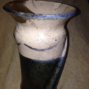 Może przedstawiać: Ręcznie wykonany ceramiczny wazon o unikalnym designie. Wazon posiada białą górną część z niebieskimi akcentami i ciemnoniebieską dolną część. Obręcz jest obrysowana na niebiesko. Wazon ma teksturowaną powierzchnię i rozszerzany otwór.
