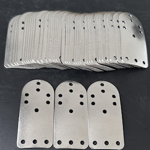 May include: A stack of silver-colored metal plates with rounded tops and multiple holes. Three plates are arranged at the bottom. These plates are likely used for furniture or construction.