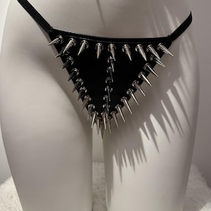 May include: Black leather thong with silver-colored metal spikes. The thong features a triangular design with multiple rows of spikes. The garment is displayed on a white mannequin.