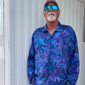 May include: A man wearing a blue and purple tie-dye long-sleeve shirt with a white hat and blue sunglasses.