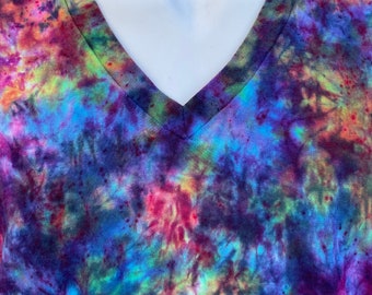 May include: A V-neck t-shirt with a vibrant tie-dye pattern. The shirt features a blend of colours, including purple, blue, pink, and green. The fabric has a soft, textured appearance.